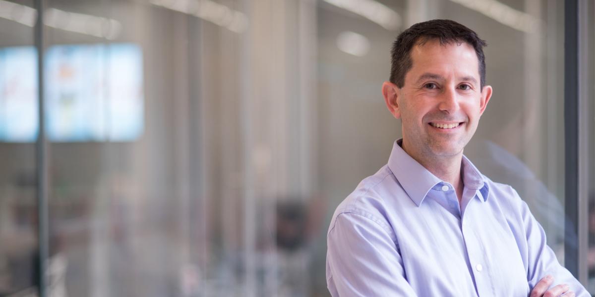 Peter Stone, who was tapped in 2019 by Sony Corp. to head up the U.S. branch of its new global artificial intelligence research division, is now also chief scientist for Sony AI. Photo credit: University of Texas at Austin. Peter Stone standing in the Gates Dell Complex in a blue button down shirt, arms crossed and smiling at camera.