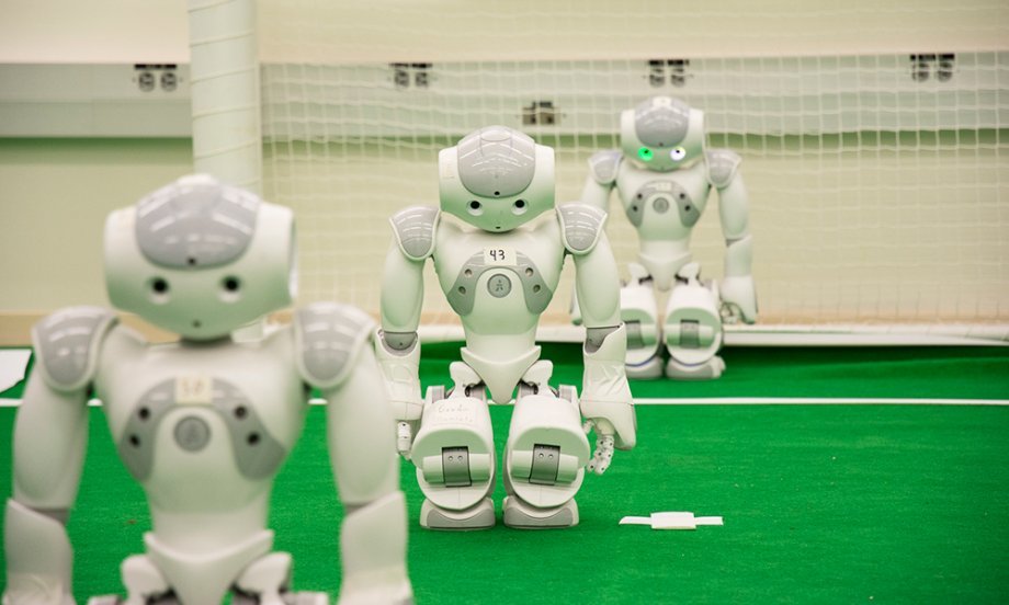 Three Nao humanoid robots lined up on RoboCup practice field.