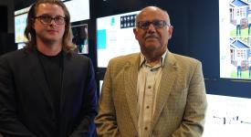 Computer scientists Ryan Farell and Chandrajit Bajaj standing side-by-side in front of the visualization wall in the POB Vis Lab.