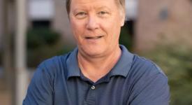 One Year After Chat GPT-4,Risto Miikkulainen Reflects on What to Know about Generative AI Risto Miikkulainen standing in front of a UT building in a blue polo style shirt with arms crossed.