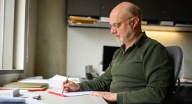 Professor David Zuckerman sitting at his desk in his office writing on a tablet of paper.
