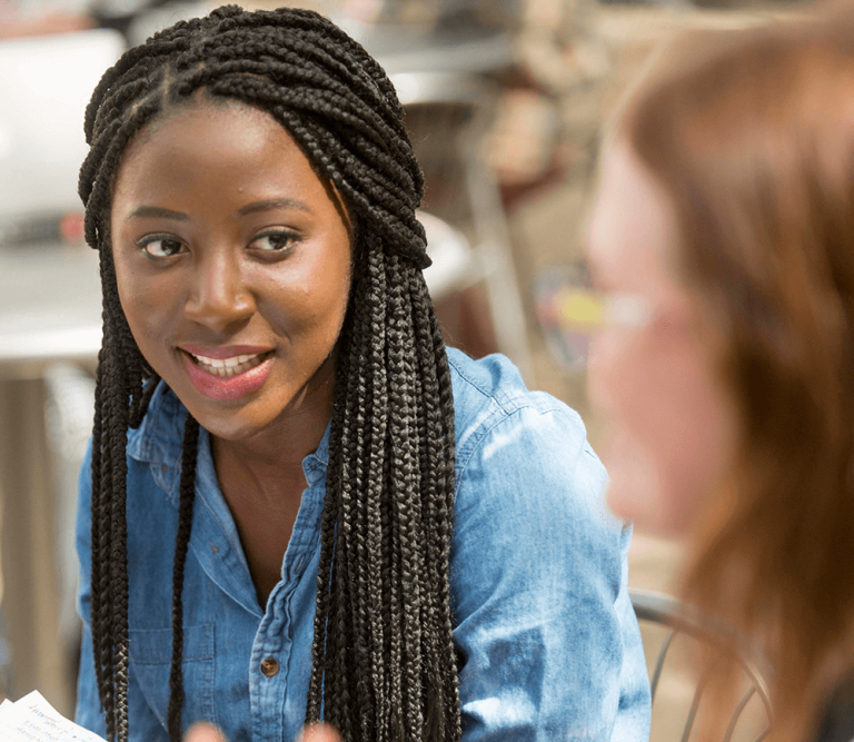A student with long braids is seated and smiling, engaged in conversation.