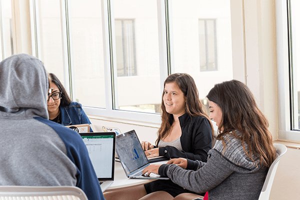 Students collaborating a table in a classroom with their laptops open