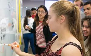 Student writing on whiteboard with marker with fellow students looking on.