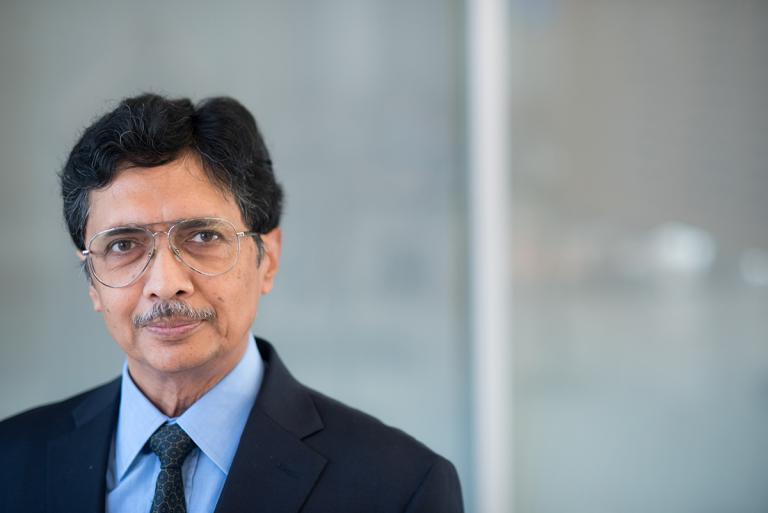 Professor Shyamal Mitra in a suit and blue button-down shirt, standing inside the GDC at UT Austin.