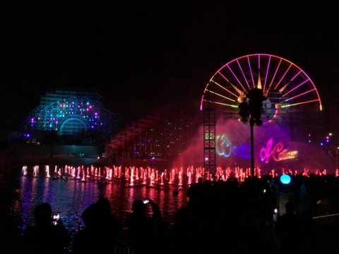Fountains colored by light and a glowing ferris wheel mark the nighttime scene.