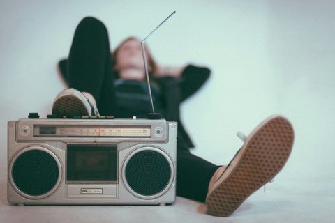 Young person lounging back with a boombox under their right foot listening to music.