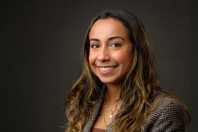 Faria Laliwala wearing a dark tan blazer, smiling at the camera.