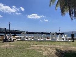 Subic Bay sign in front of the bay.  Alan sitting on bench